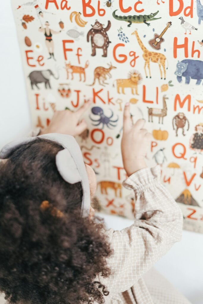 A child points at an educational alphabet and animal poster indoors.